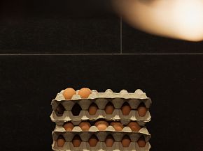 Stapel von Eierkartons mit braunen Eiern, gestapelt auf einem dunklen Hintergrund in einer modernen Küche.