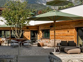Gemütliche Hotelterrasse mit Holzmöbeln, grünen Sonnenschirmen und Panoramablick auf bewaldete Berge. Einladende Atmosphäre für entspannte Momente.